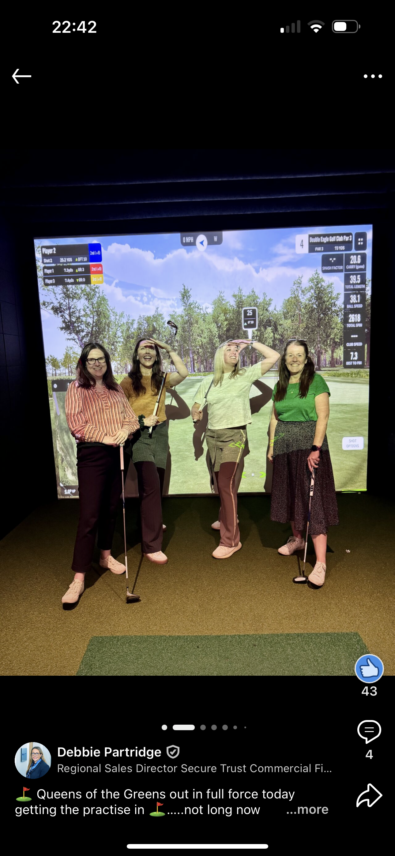 Four women posing in front of a golf simulator screen. They are holding golf clubs, with various expressions, in a practice room.