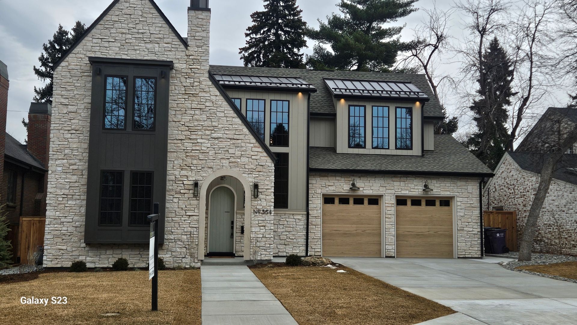 A two-story stone house with a dark brown trim, an arched front door, and a two-car garage under a gray sky.