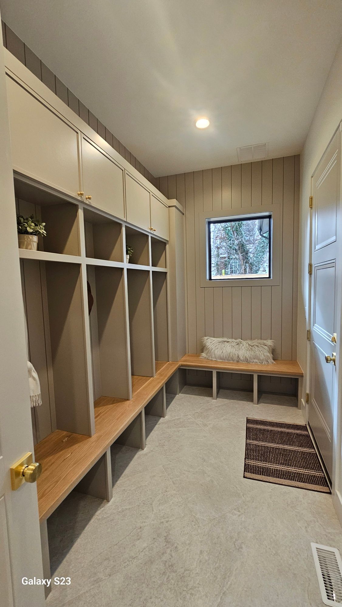 A mudroom with built-in lockers, a wooden bench, a small window, and a patterned rug.