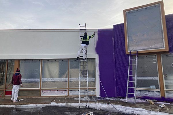 A man is painting the side of a building with purple paint.