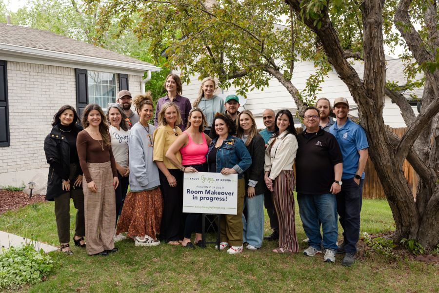 Group of people pose outside a house, holding a sign.