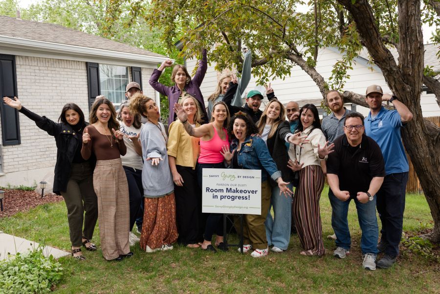 Group of people posing outdoors with arms raised, in front of a house. Sign reads "House Makeover in progress."