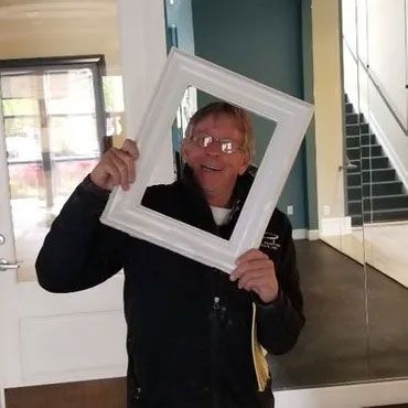 A man in a black jacket is holding a white picture frame.