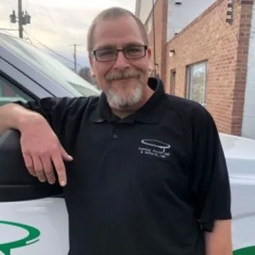 A man with glasses and a beard is leaning against a white van.