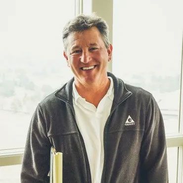 A man is standing in front of a window holding a book and smiling.
