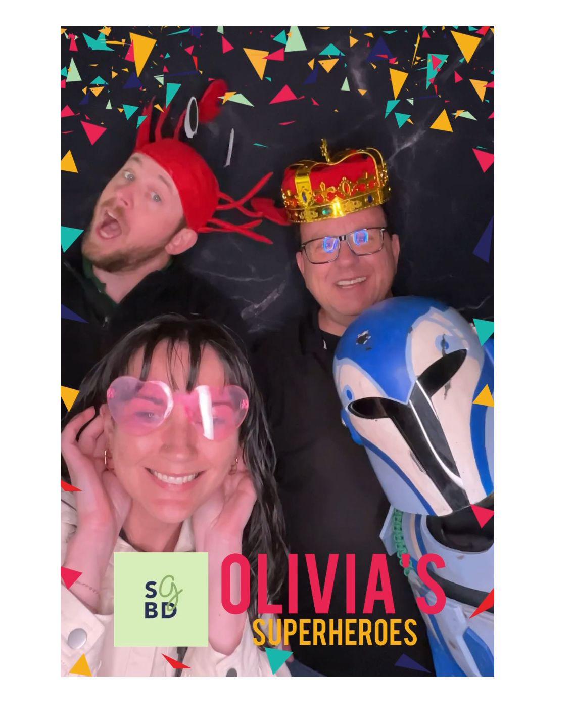 Four people in costumes and props posing for a photo booth. Includes a crown, goggles, and a superhero mask.