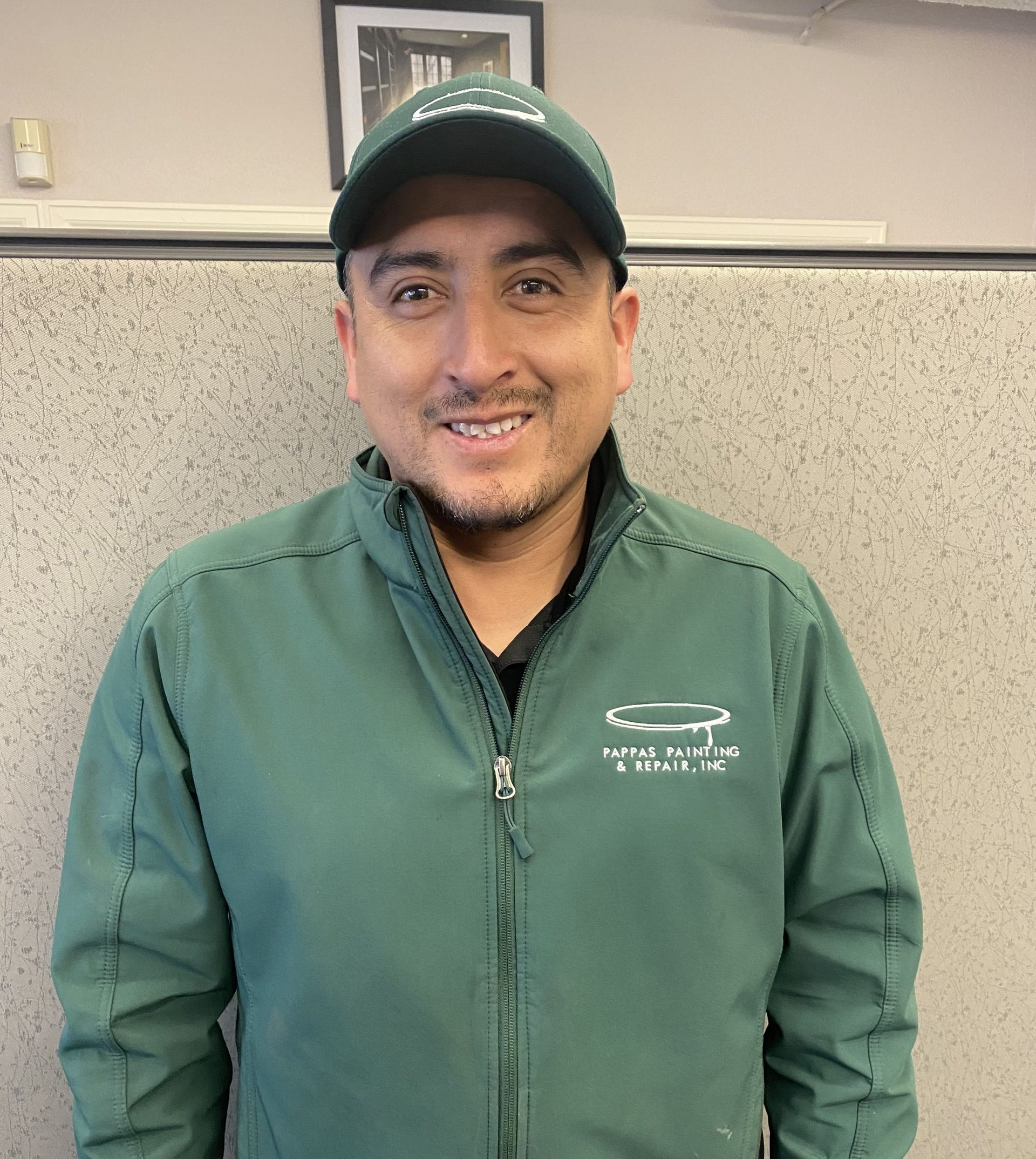 A man in a green jacket and hat is smiling for the camera.
