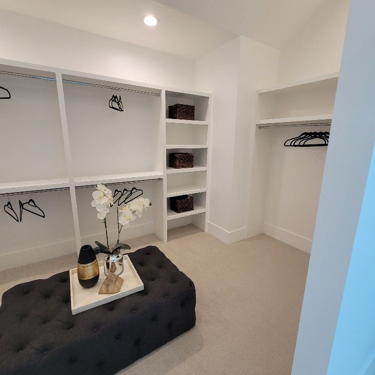 A walk in closet with a black ottoman and a vase of flowers on a tray.