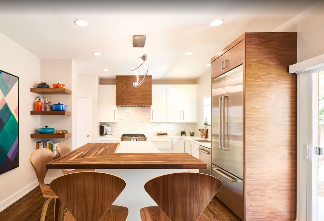 Modern kitchen featuring a wooden island with bar stools, stainless steel refrigerator, and open wall shelving.