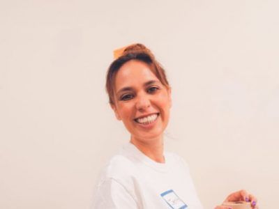 A woman in a white shirt is smiling and holding a card.