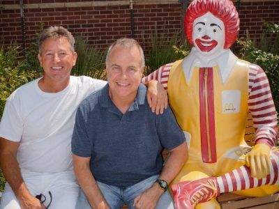 Two men are posing for a picture next to a mcdonald 's statue
