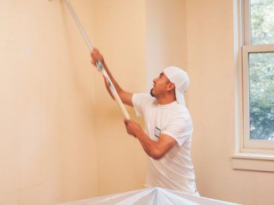 A man is painting a wall with a paint roller.