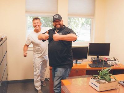 Two men are giving a thumbs up in an office.