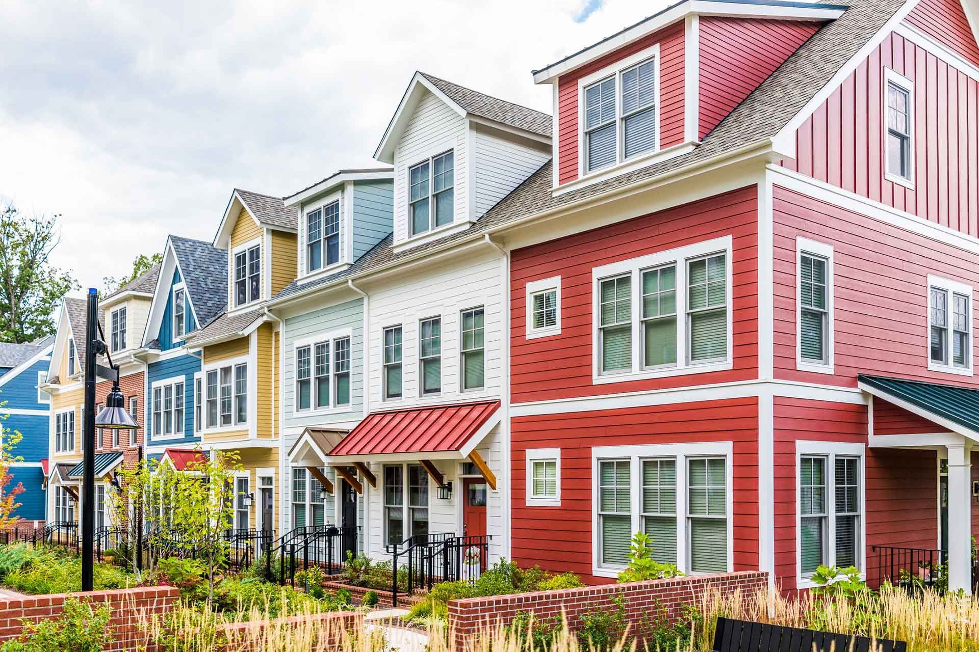 A row of colorful, multi-story townhomes with shingled siding, dormer windows, and a landscaped front yard.