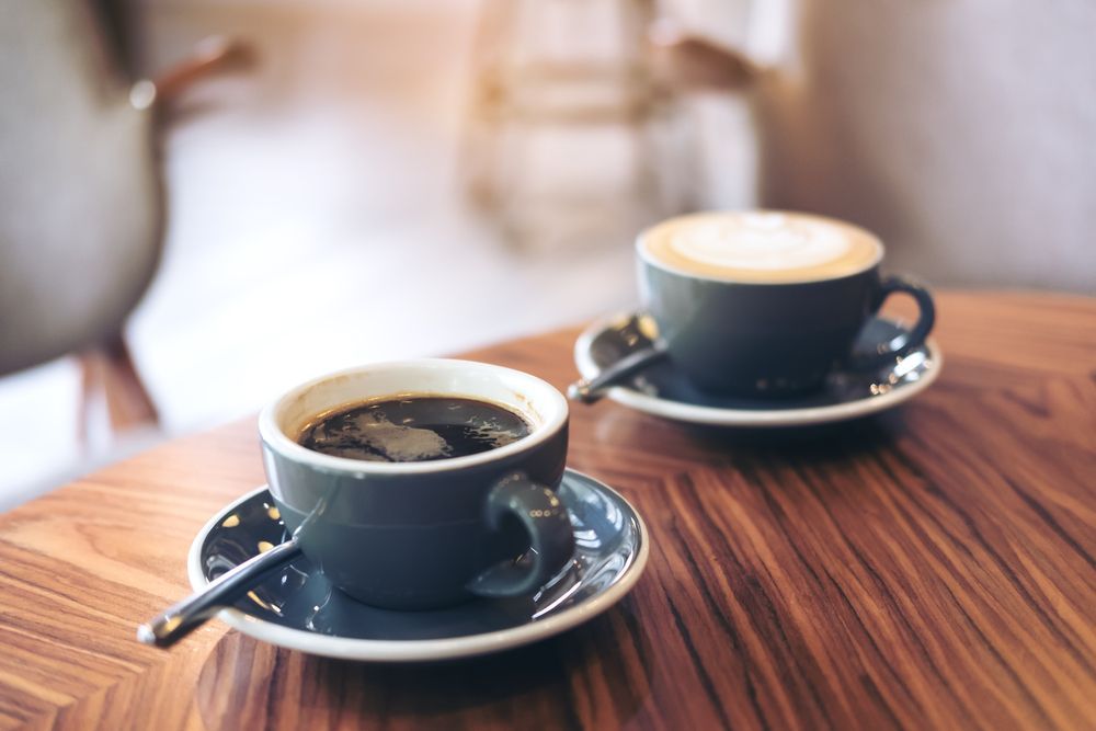 Two coffee cups with saucers on a wooden table; one black coffee, one latte.
