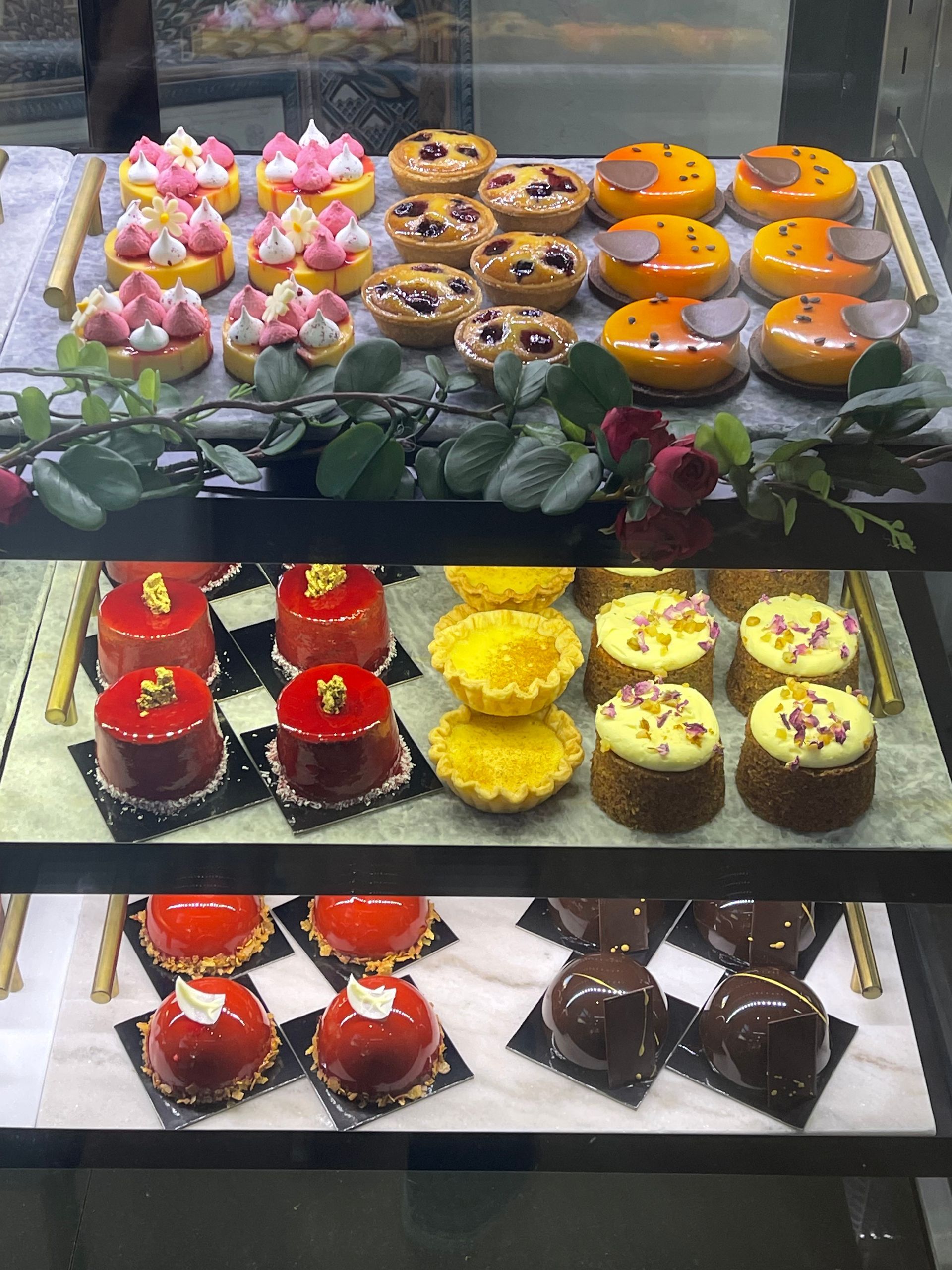 Pastries displayed in a glass case. Rows of colorful tarts and cakes with various toppings.