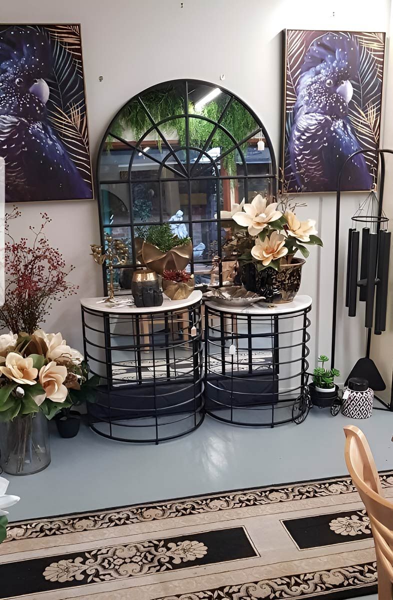 Interior design display with an arched mirror, two side tables, and floral arrangements.