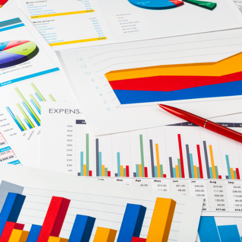 A pen sits on top of a pile of graphs and charts including one that says expenses