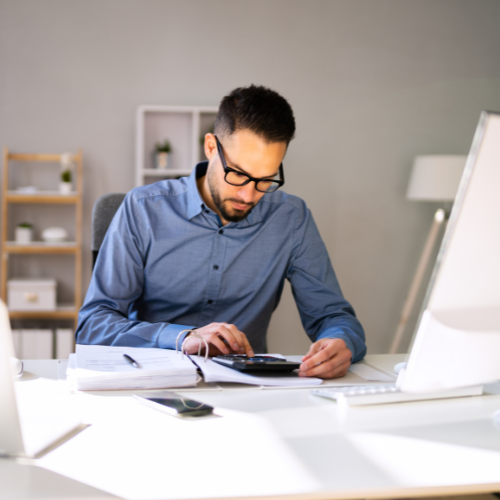 A man is sitting at a desk using a calculator
