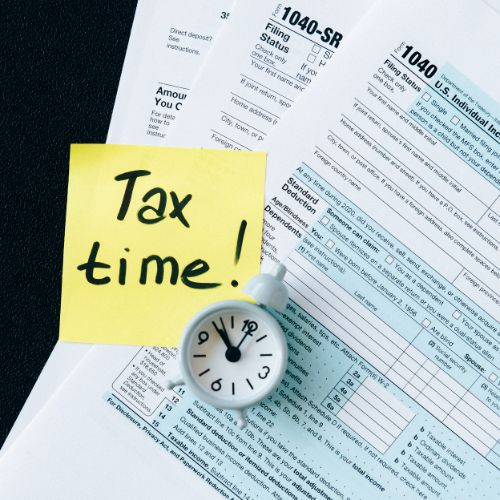 A clock sits next to a sticky note that says tax time