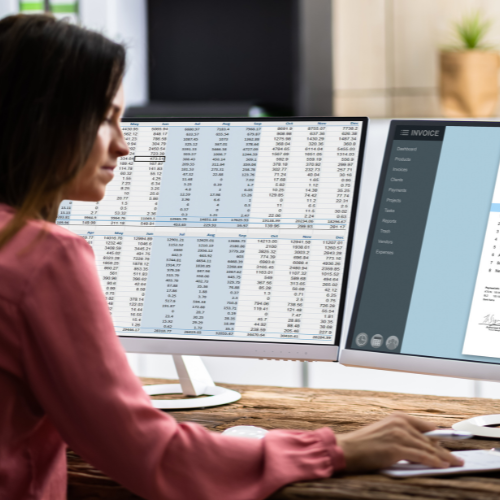 A woman is sitting in front of two computer monitors.