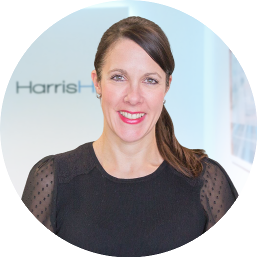 Woman in black top smiles, standing in front of the HarrisHills logo.