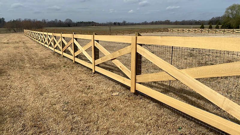 Wooden fence in a field with crisscross design and posts. The sky is overcast.