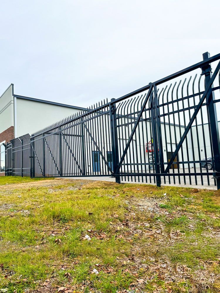 Black metal security fence with a building in the background. The fence has vertical bars with curved tops and a gate.
