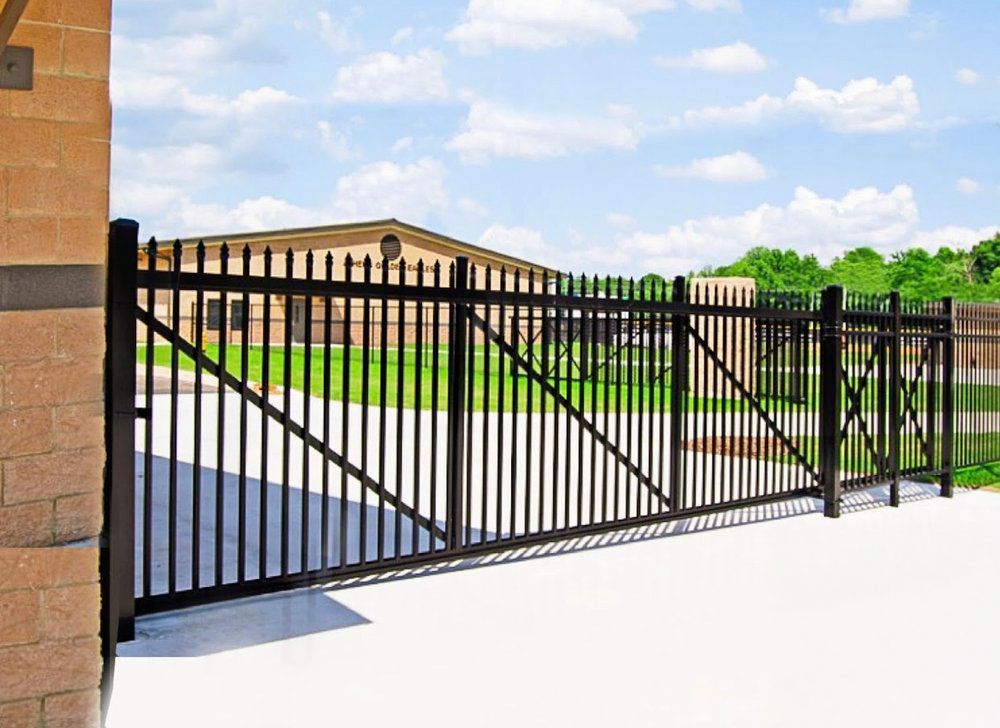 Black metal gate in front of a brick building, set against a sky with clouds.
