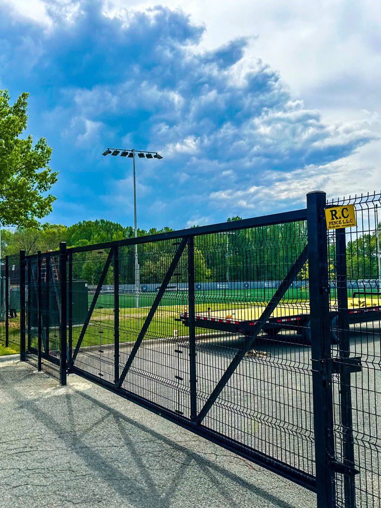 Black metal gate in front of a field, under a cloudy sky. A yellow sign with 