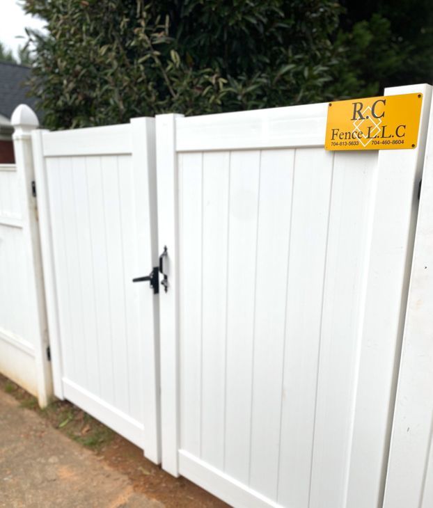 White vinyl fence with a gate and a black handle. A yellow sign says 