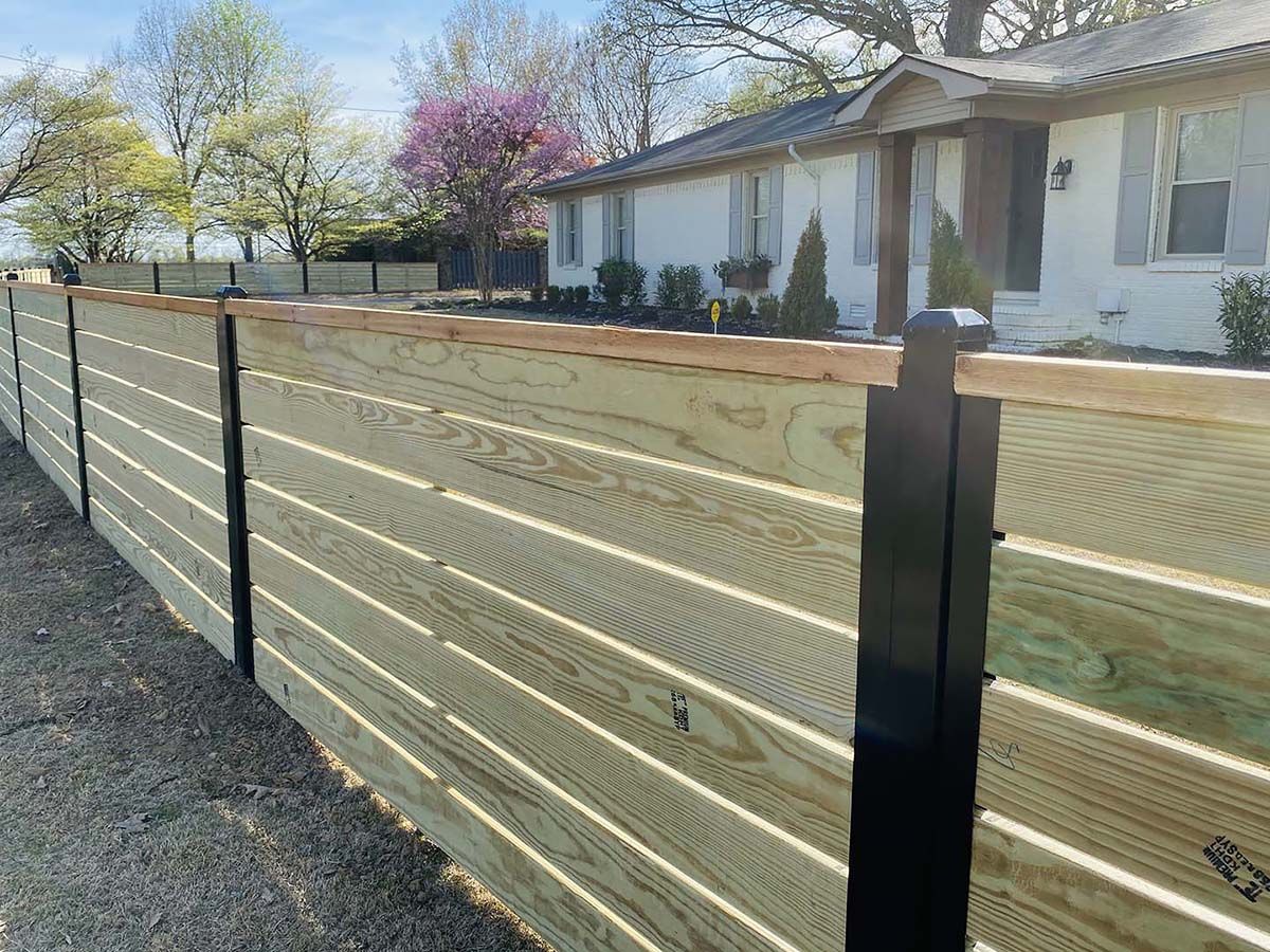 Wooden horizontal slat fence in front of a white house on a sunny day.
