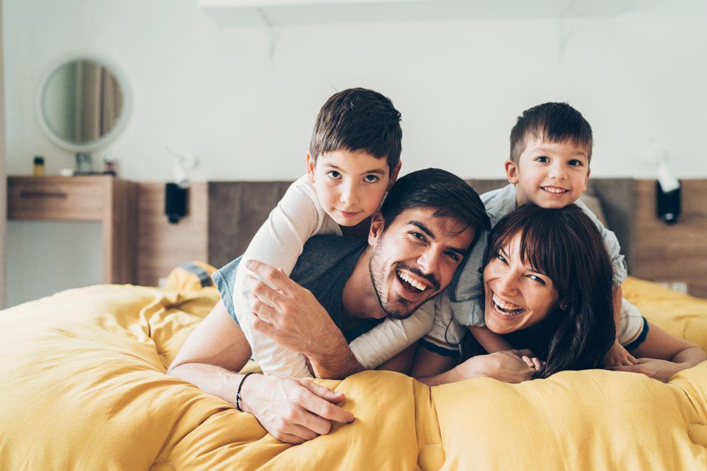 Smiling Family Lying On The Bed — Aurora, CO — Katherine Moskal Health Plans Smiling Family Lying On The Bed — Aurora, CO — Katherine Moskal Health Plans