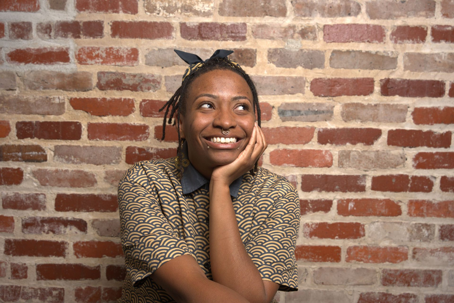 Person smiling with chin on hand against a brick wall backdrop