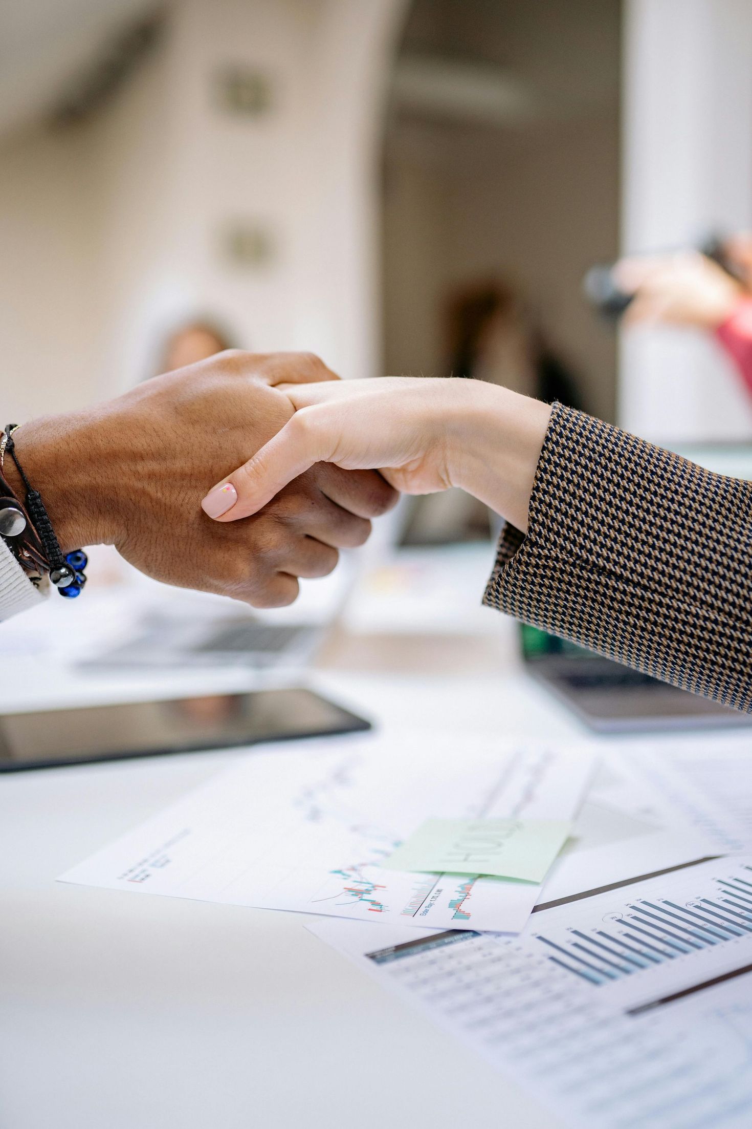 Two people shake hands over a desk with charts and papers, suggesting a business agreement.