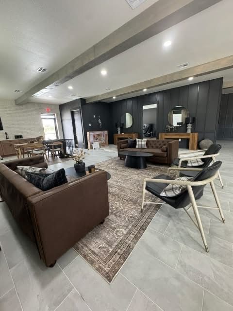 Modern lounge with brown sofas, black chairs, coffee tables, and a kitchen/bar area under recessed lighting