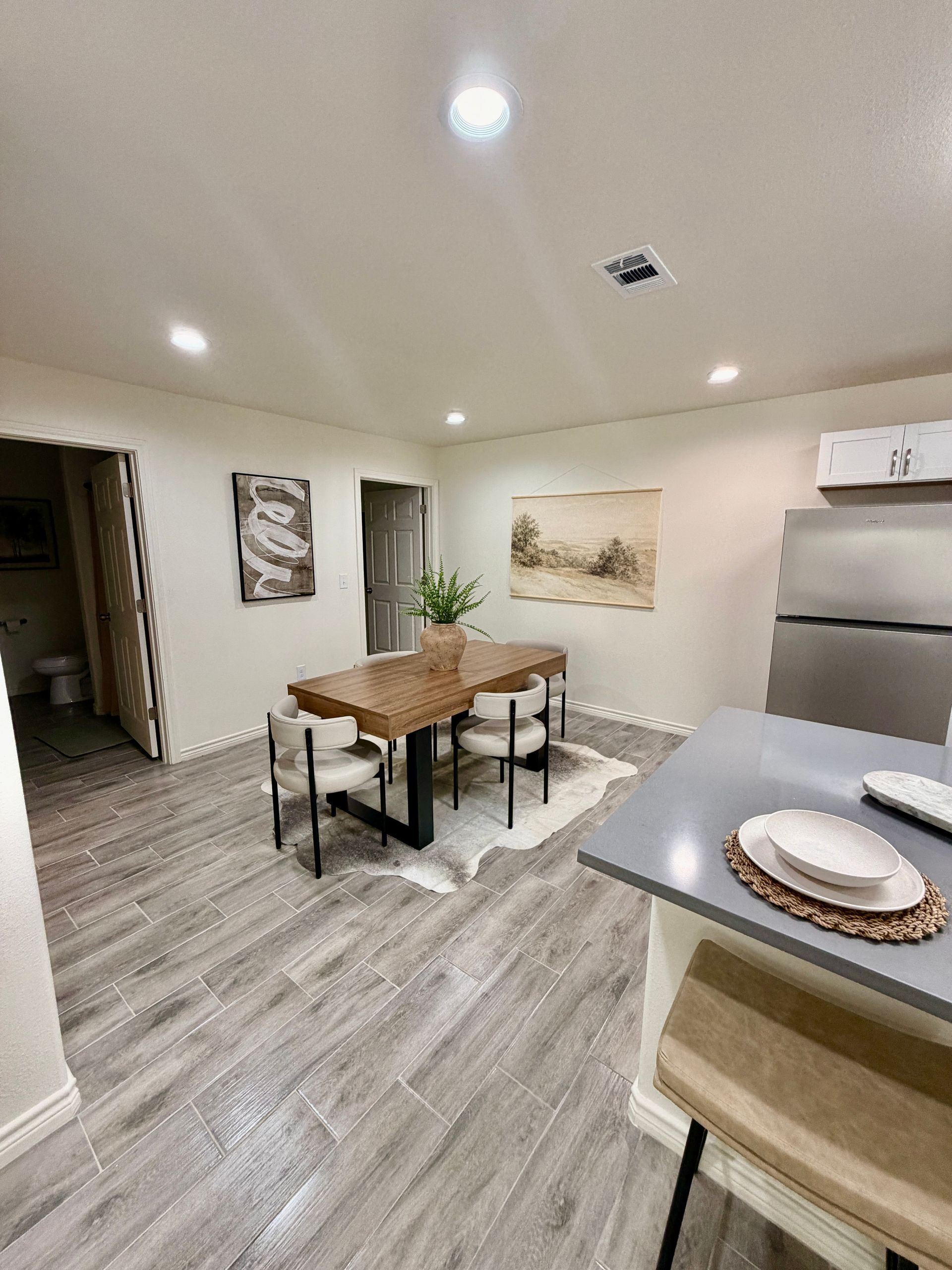 Bright kitchen-dining area with wooden table, gray flooring, and stainless steel appliances.
