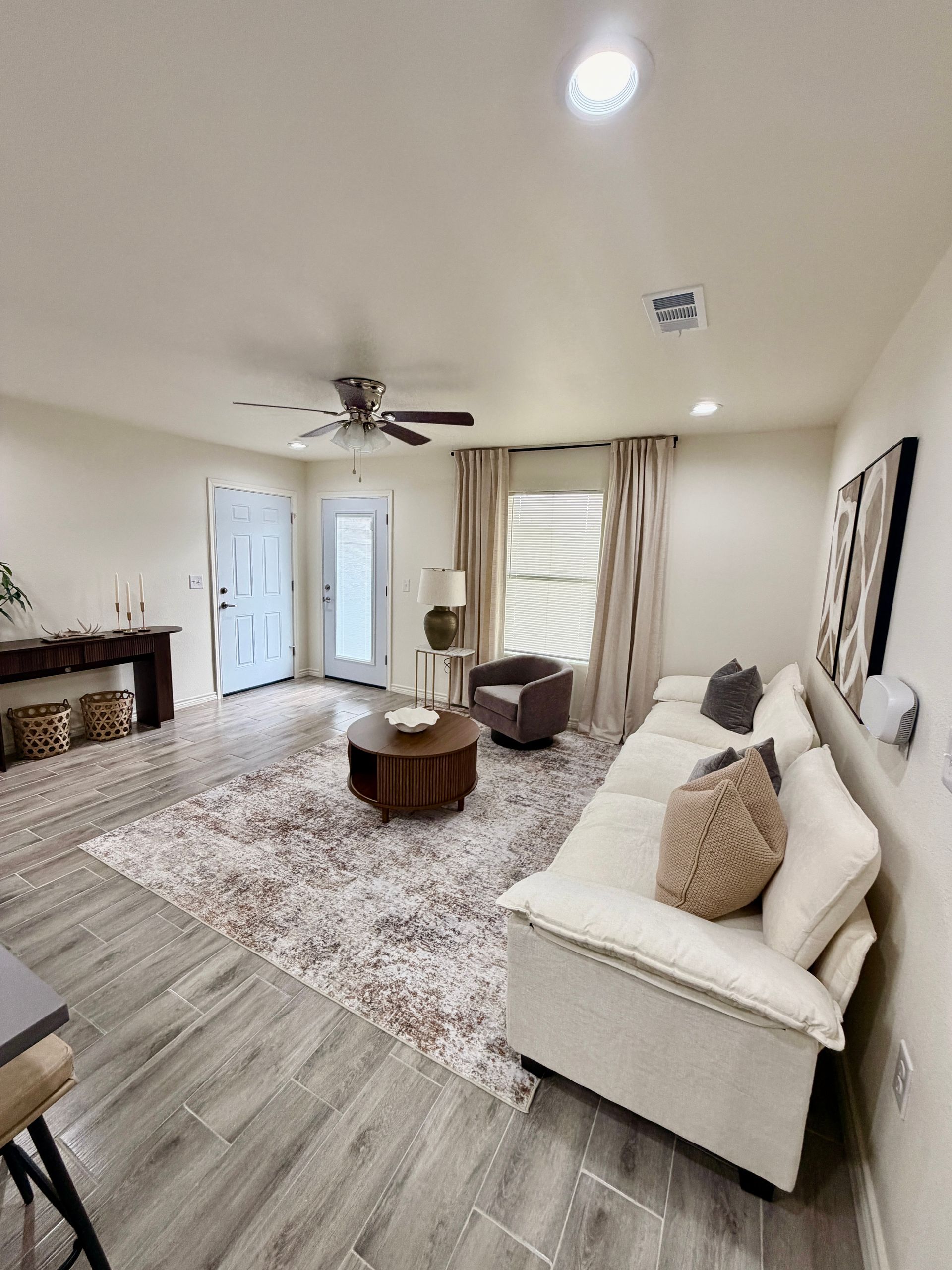 Bright living room with white sofa, coffee table, fireplace, ceiling fan, and large windows with curtains