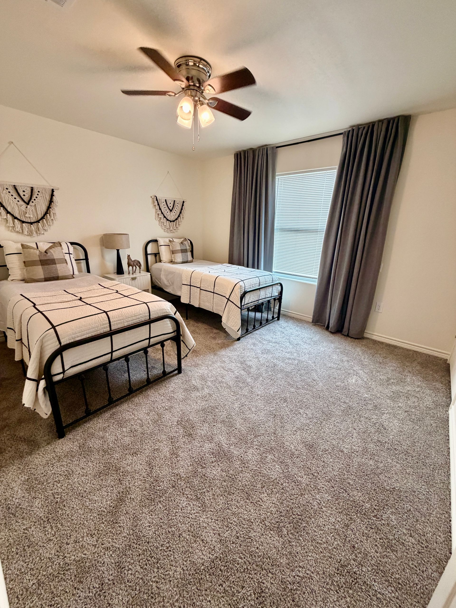 Carpeted bedroom with two twin beds, gray curtains, ceiling fan, and a sliding glass door.