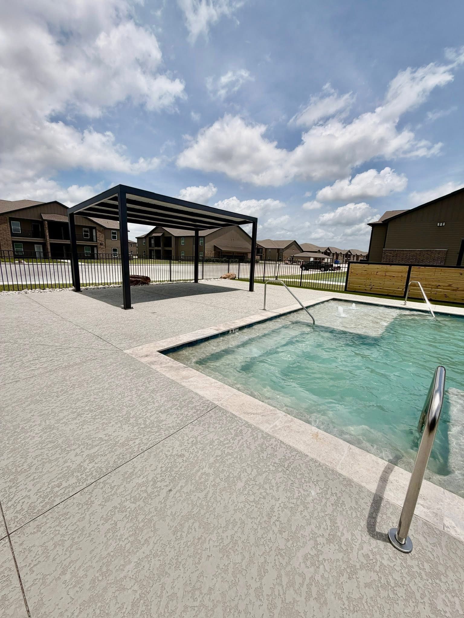 Outdoor pool with a pergola, lounge chairs, and a cloudy sky over a light gravel deck.
