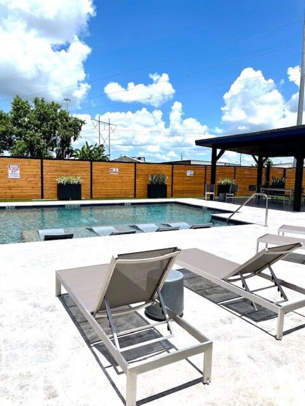 Poolside lounge chairs beside a small outdoor pool under a bright blue sky with clouds.