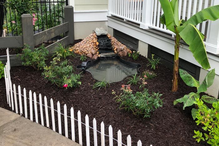A white picket fence surrounds a garden that may need fence repair