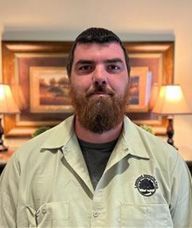 A man with a beard is wearing a green shirt and standing in front of a painting.