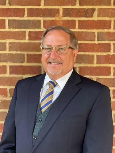 An older man in a suit with glasses smiling.