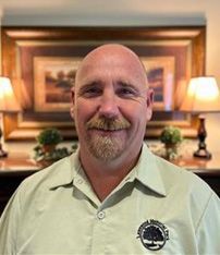 A bald man with a beard is smiling for the camera in front of a picture.