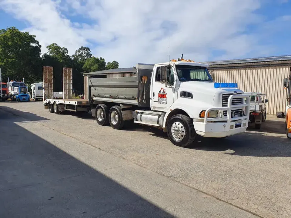 A White Dump Truck With a Trailer Parked in a Gravel Lot — Mid North Coast Heavy Vehicle Repairs In Laurieton, NSW