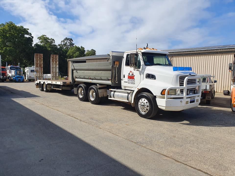 A White Dump Truck With a Trailer Parked in a Gravel Lot — Mid North Coast Heavy Vehicle Repairs In Lake Cathie, NSW