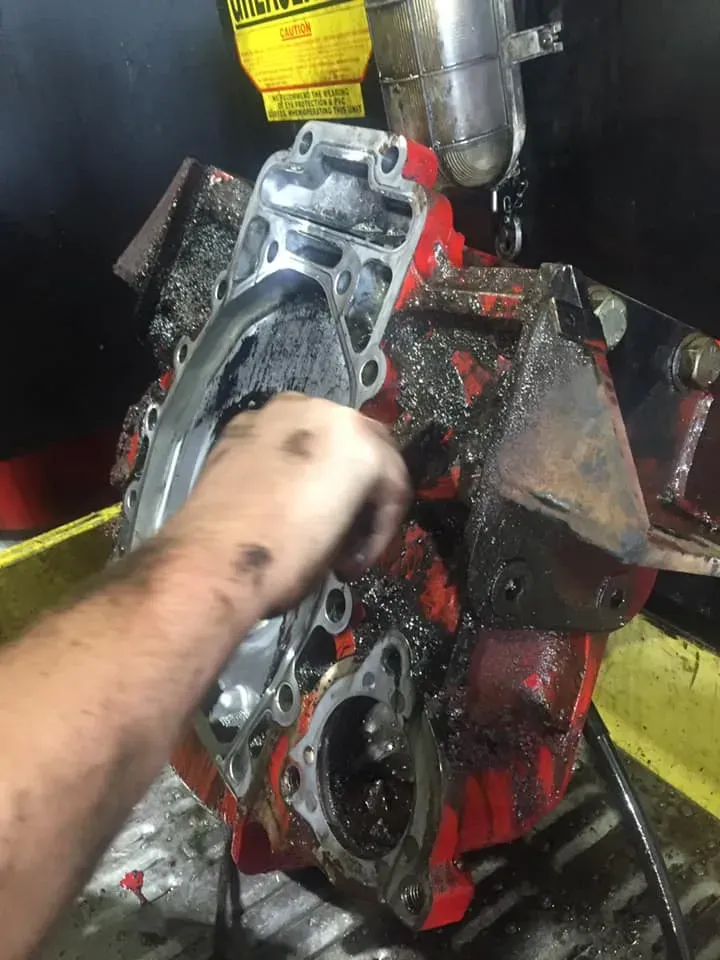A Person’s Hand Cleans a Grease-covered, Red Mechanical Engine Part — Mid North Coast Heavy Vehicle Repairs In Kempsey, NSW