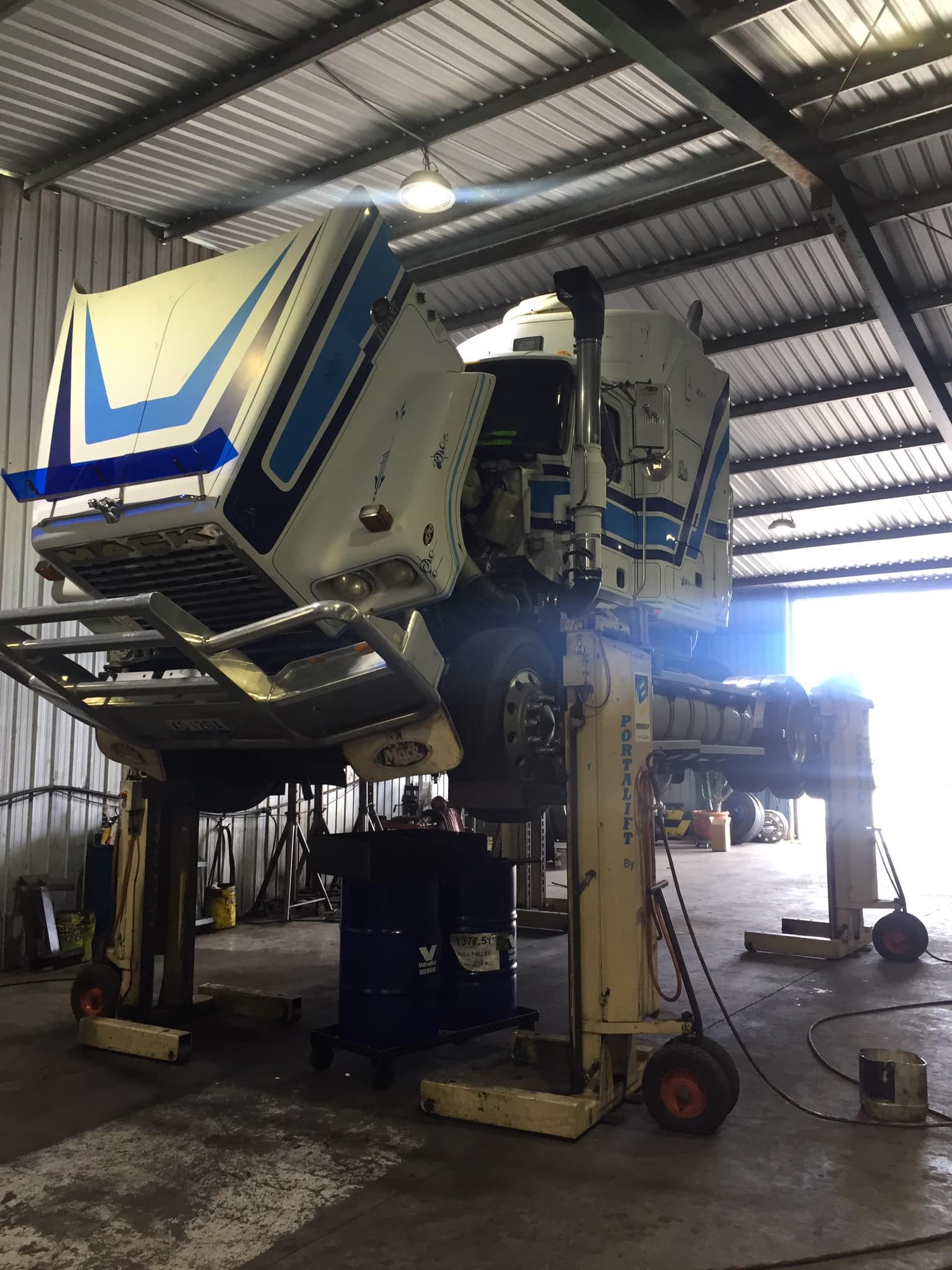A White and Blue Semi-truck Cab Lifted High in a Repair Shop — Mid North Coast Heavy Vehicle Repairs In Taree, NSW