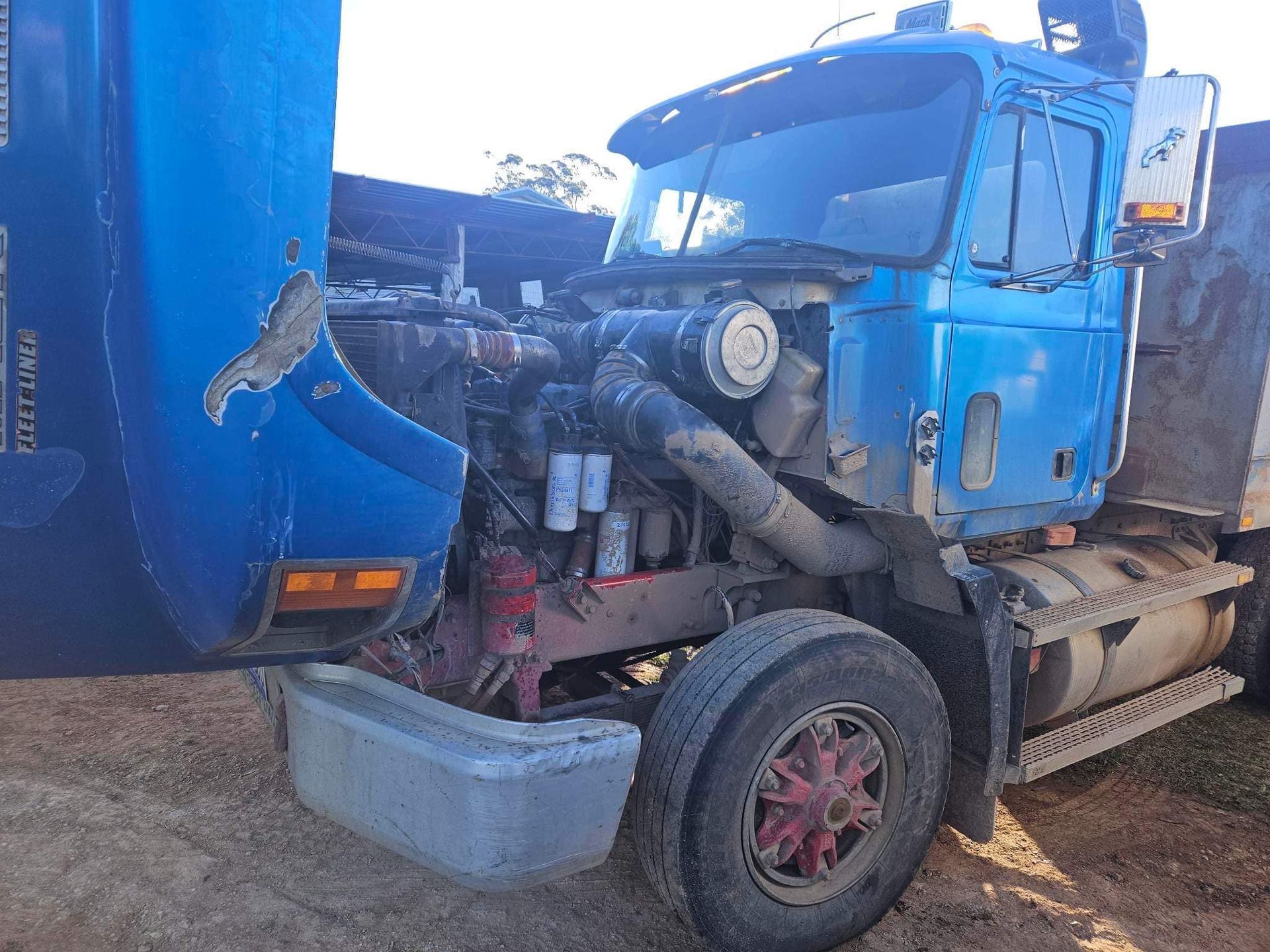 A Blue Dump Truck Sits on Dirt With Its Hood Flipped Forward — Mid North Coast Heavy Vehicle Repairs In Kempsey, NSW